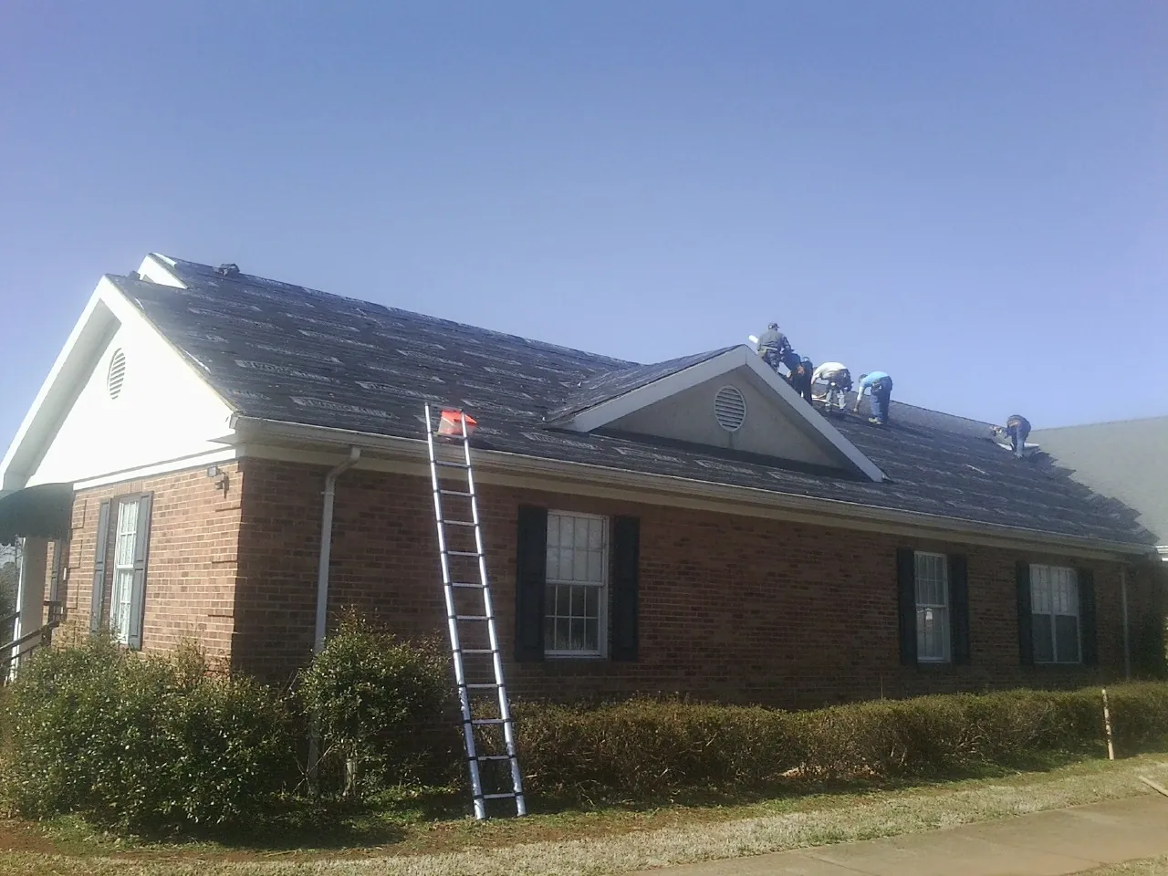 Crew tearing shingles off a brick ranch roof with a ladder set — Emergency Roof Repair work by our crew in Bellevue
